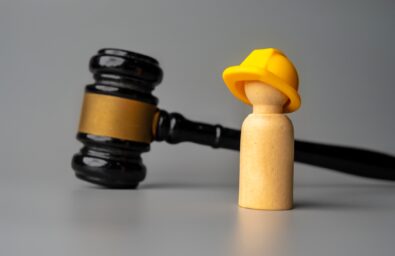 A wooden doll wearing a hard hat stands in front of a gavel. Construction law, worker safety, or legal disputes in the construction industry concept.
